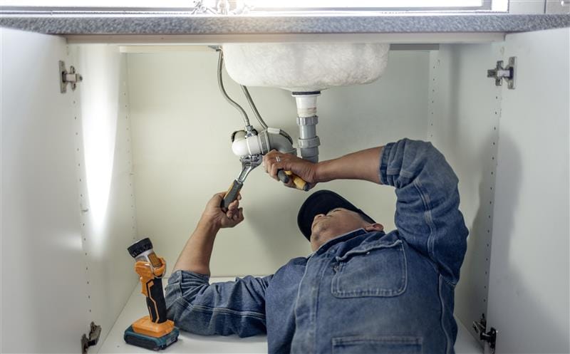 Plumber repairing pipes beneath a bathroom sink in Brentwood