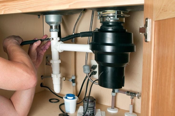Plumber installing a garbage disposal beneath a kitchen sink in Brentwood