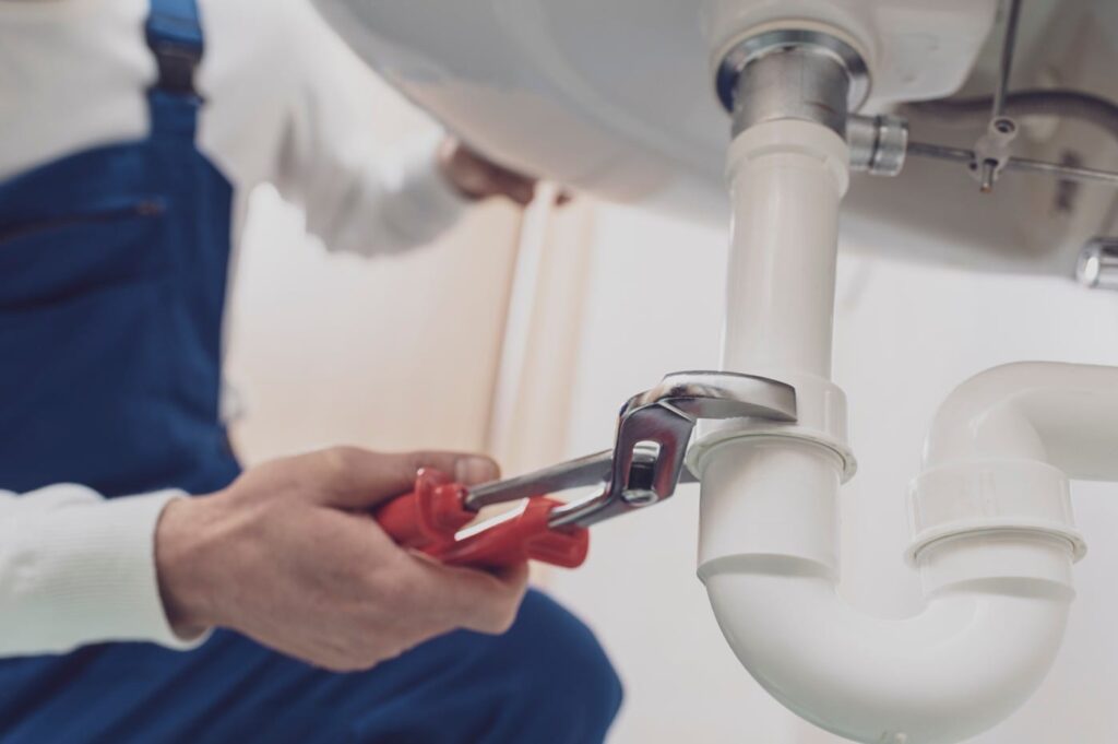 Plumber repairing a white drain pipe beneath a sink in Brentwood
