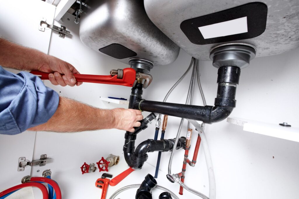 Plumber repairing drain pipes beneath a kitchen sink in Brentwood